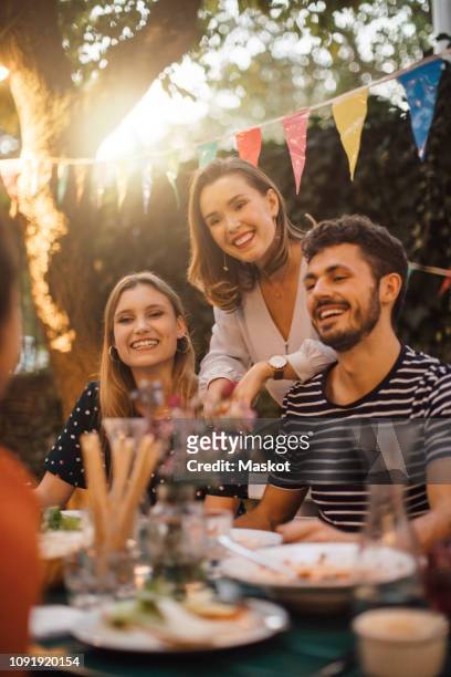 happy young male and female friends at table during dinner party in backyard - standing table outside stock pictures, royalty-free photos & images
