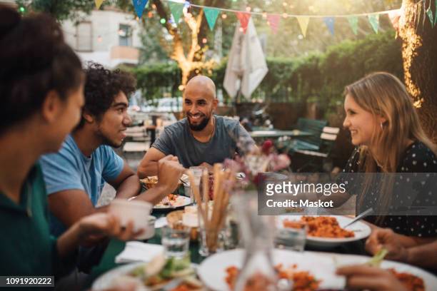 smiling young man and women listening to male friend talking during dinner party in backyard - dinner party stock pictures, royalty-free photos & images