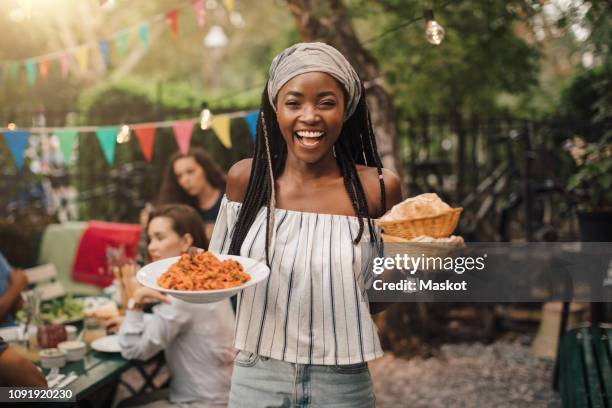 portrait of smiling young woman carrying food while standing in backyard during garden party - garden party stock-fotos und bilder