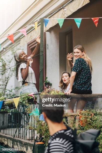 happy young women waving hands at male friend while standing in balcony during party - friends waving stock pictures, royalty-free photos & images