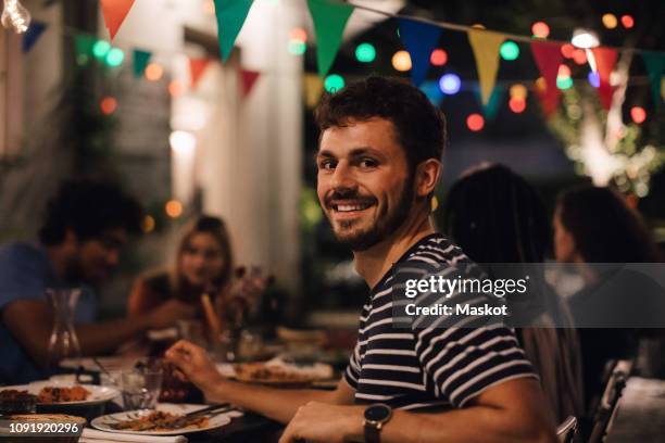 portrait of smiling young man having dinner with friends during garden party - 19 years old dinner stock pictures, royalty-free photos & images