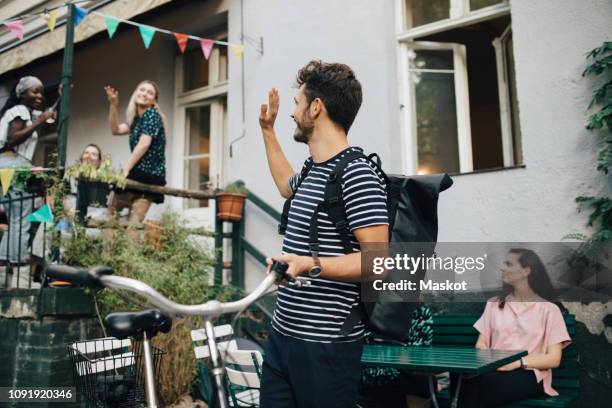 smiling young man waving hand while standing with bicycle in backyard - friends waving stock pictures, royalty-free photos & images