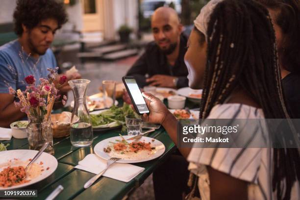 young woman using smart phone while having dinner with friends during garden party - evening meal restaurant stock pictures, royalty-free photos & images