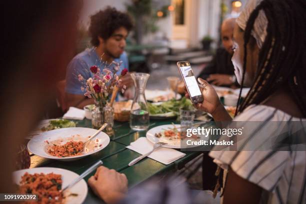 young woman using mobile phone while having dinner with friends during garden party - 19 years old dinner stock pictures, royalty-free photos & images