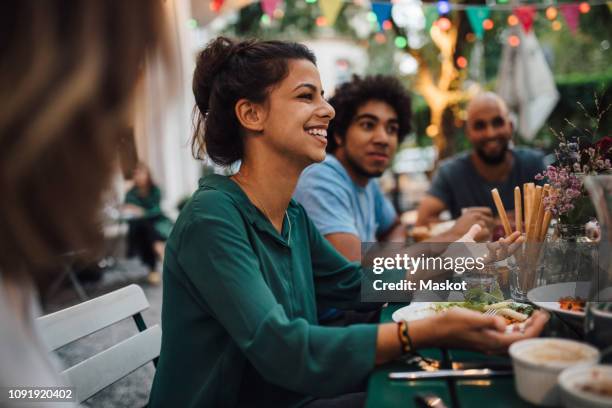 smiling young women gesturing while sitting with friends at table during dinner party - outdoor dinner party stock pictures, royalty-free photos & images