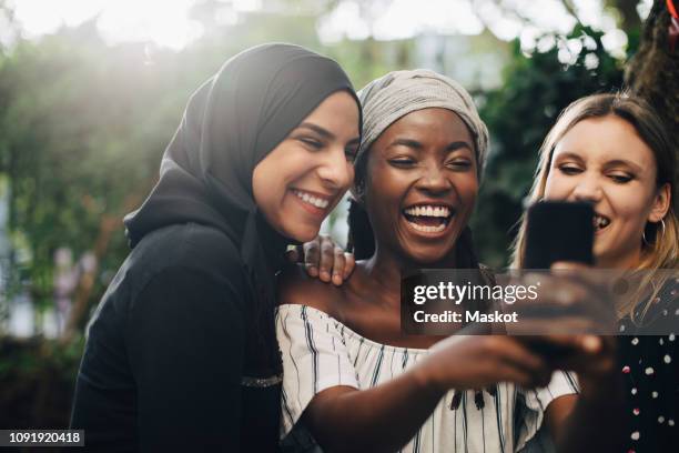 smiling multi-ethnic female friends taking selfie through mobile phone in backyard - wedding veil stock-fotos und bilder