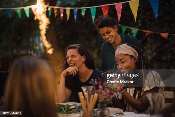 cheerful multi-ethnic friends enjoying at table during dinner party in backyard - home party foto e immagini stock