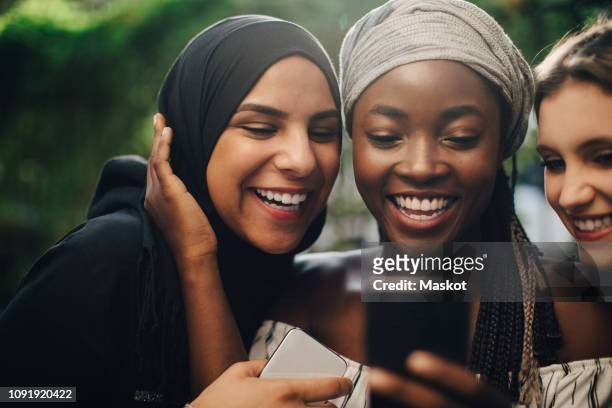 smiling multi-ethnic friends looking at mobile phone while standing in backyard - vorderasiatische abstammung stock-fotos und bilder