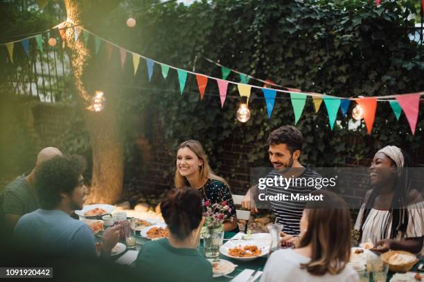 multi-ethnic young friends enjoying dinner at table during garden party - gartenparty stock-fotos und bilder
