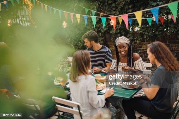 young male and female friends enjoying food at table during dinner party in backyard - 19 years old dinner stock pictures, royalty-free photos & images