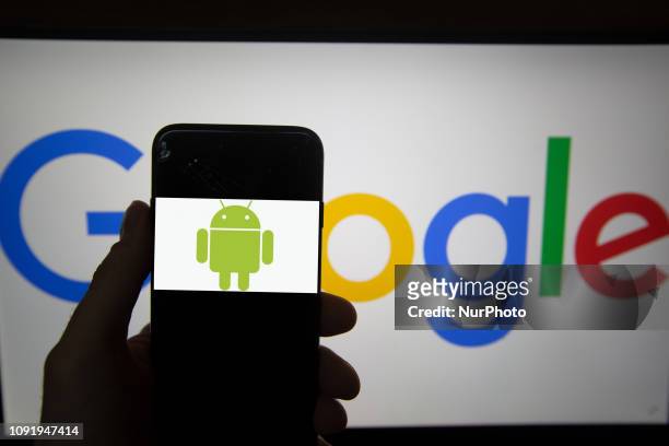 The logo of Android is seen on a screen. In the background there is the logo of Google. Alphabet is the mother company of Google. It has a revenue of...