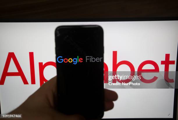 The logo of Google Fiber is seen on a screen. In the background there is the logo of Alphabet. Alphabet is the mother company of Google. It has a...