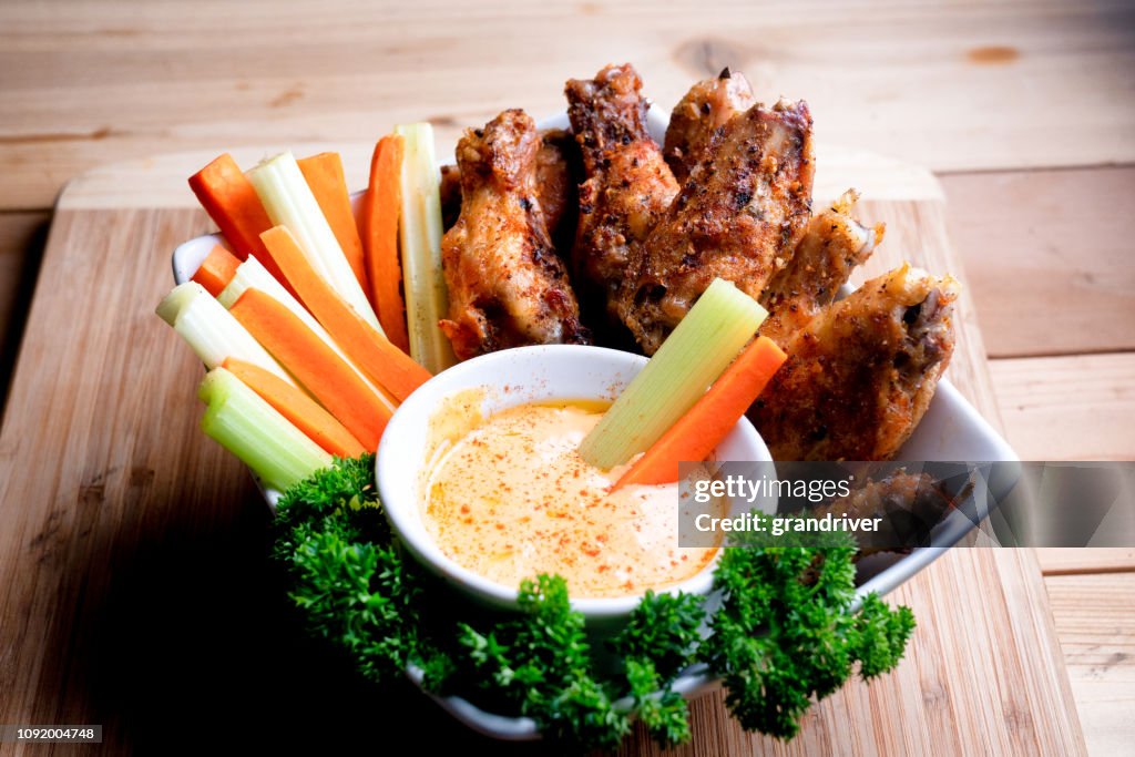 A Bowl Of Healthy Baked Grilled Chicken Wings Accompanied By Hot Sauce Celery and Carrot Sticks