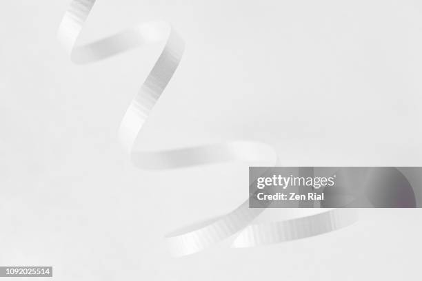 close up of a single curled white ribbon against white background - white ribbon stock pictures, royalty-free photos & images