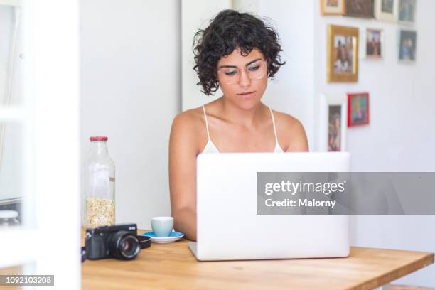 young woman sitting in the kitchen working on her laptop. - creative director stock-fotos und bilder