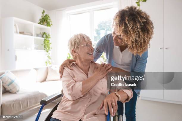 fröhliche krankenschwester kümmert sich um ältere dame - charity tin stock-fotos und bilder