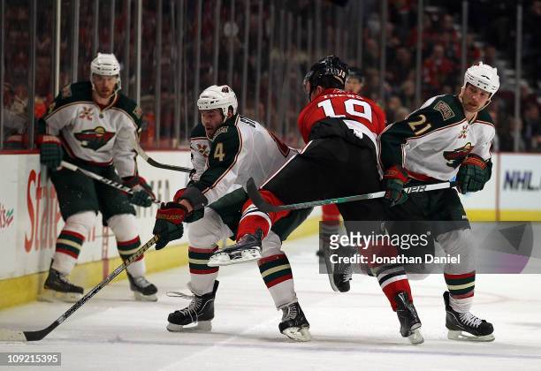 Clayton Stoner and Kyle Brodziak of the Minnesota Wild squeeze out Jonathan Toews of the Chicago Blackhawks as Stoner tries to control the puck at...