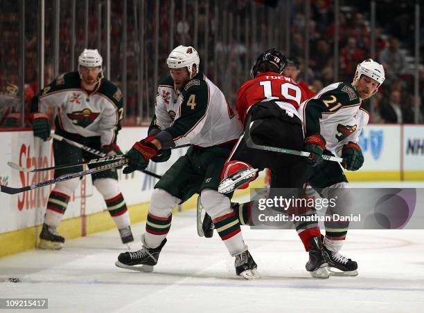 Clayton Stoner and Kyle Brodziak of the Minnesota Wild squeeze out Jonathan Toews of the Chicago Blackhawks as Stoner tries to control the puck at...