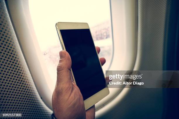 man's hand holding a mobile phone inside an airplane. - plane taking off stock pictures, royalty-free photos & images