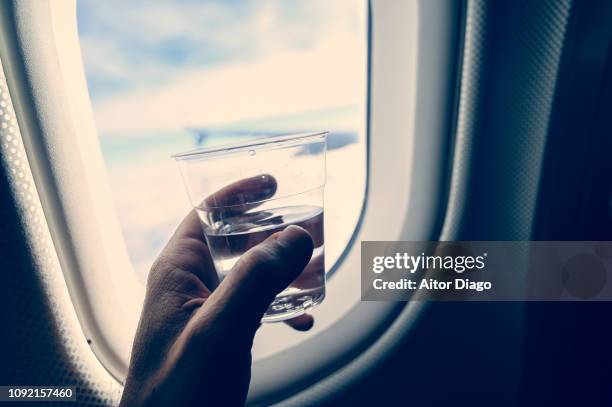 man's hand holding a glass with transparent liquid (water or liquor). inside an airplane. - glass of water hand ストックフォトと画像