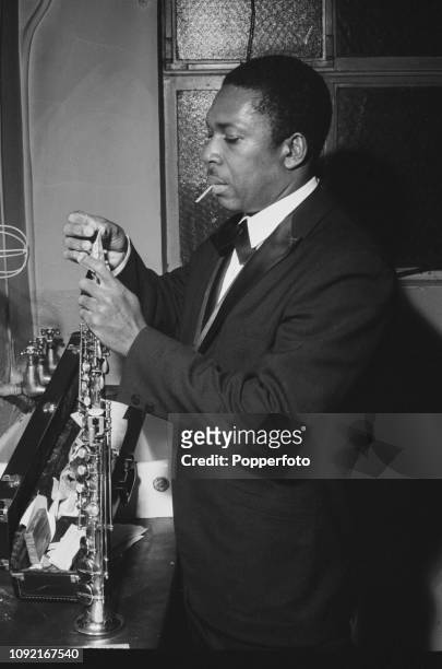 American jazz saxophononist, composer and musician John Coltrane pictured changing a reed on his soprano saxophone in a dressing room backstage prior...