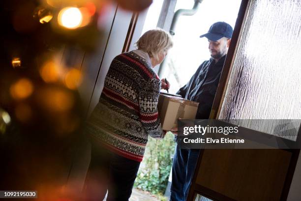 senior woman signing for christmas packages delivered by postman - answering door stock pictures, royalty-free photos & images