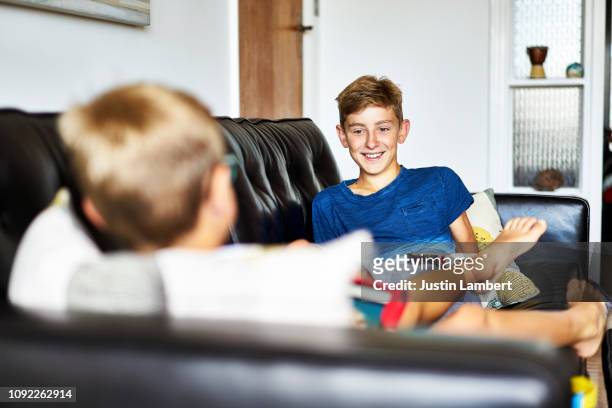 young teenager looks at brother sharing a joke sitting on the sofa - saltdean stock pictures, royalty-free photos & images
