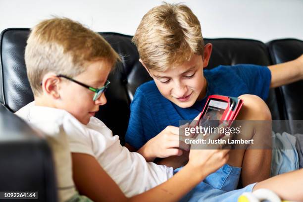 boys looking at a tablet together sharing a moment on the sofa at home - saltdean stock pictures, royalty-free photos & images