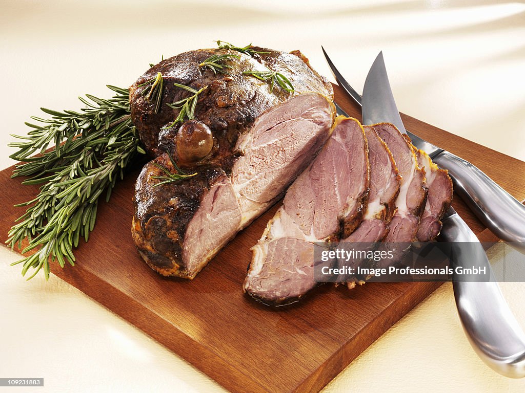 Partially sliced roast leg of lamb on chopping board