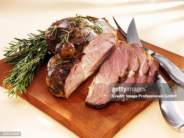 partially sliced roast leg of lamb on chopping board - leg of lamb stock pictures, royalty-free photos & images