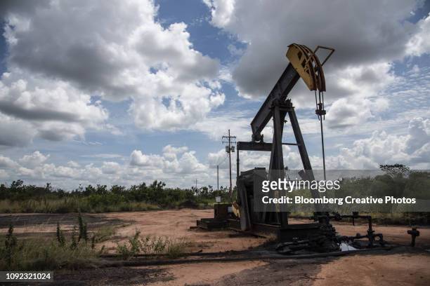 a pump jack stands near an oil spill at a facility - venezuela stock pictures, royalty-free photos & images
