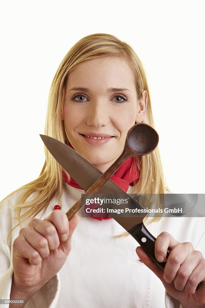 Female chef holding kitchen knife and wooden spoon, close-up, smiling