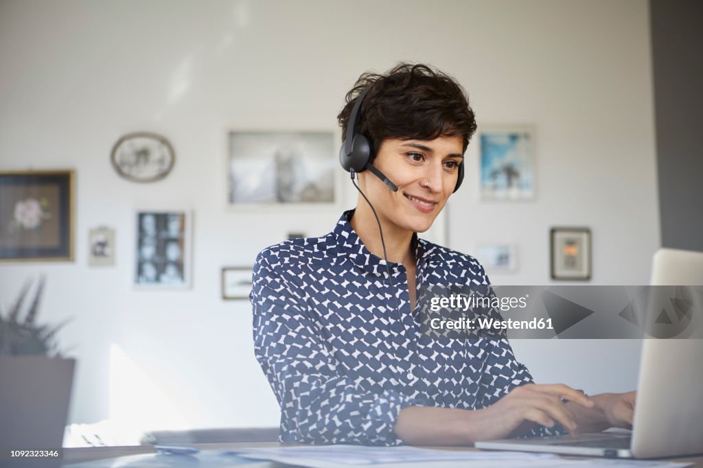 Smiling woman at home with headset using laptop