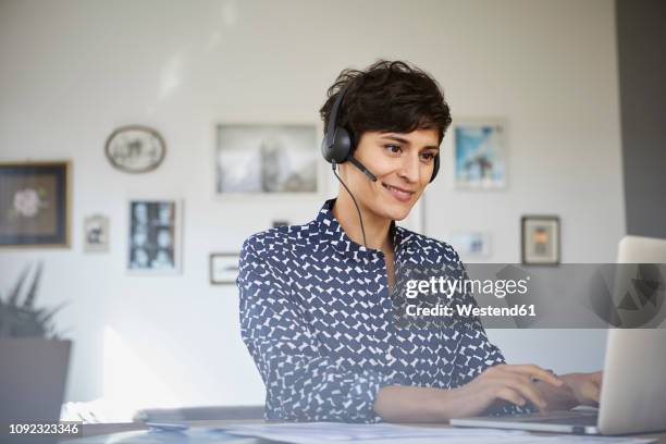 smiling woman at home with headset using laptop - headset imagens e fotografias de stock