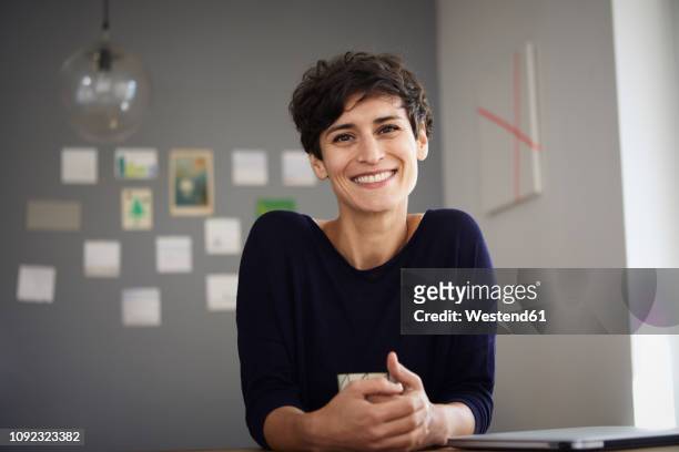 portrait of smiling woman sitting at table at home - short hair stock pictures, royalty-free photos & images