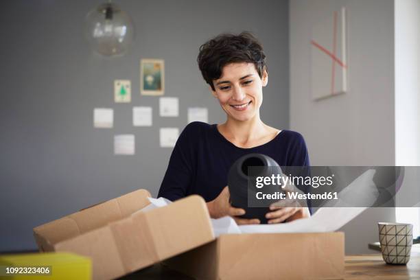 smiling woman unpacking parcel at home - auspacken stock-fotos und bilder
