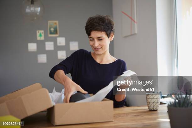 smiling woman packing parcel at home - receiving stock-fotos und bilder