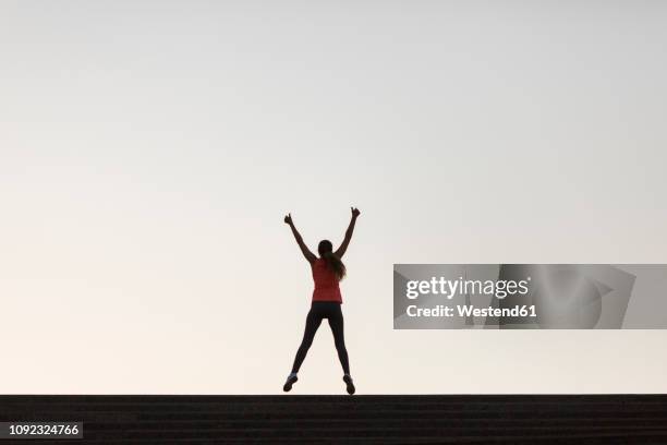 rear view of successful sportswoman raising her arms - woman leaping silhouette stock pictures, royalty-free photos & images