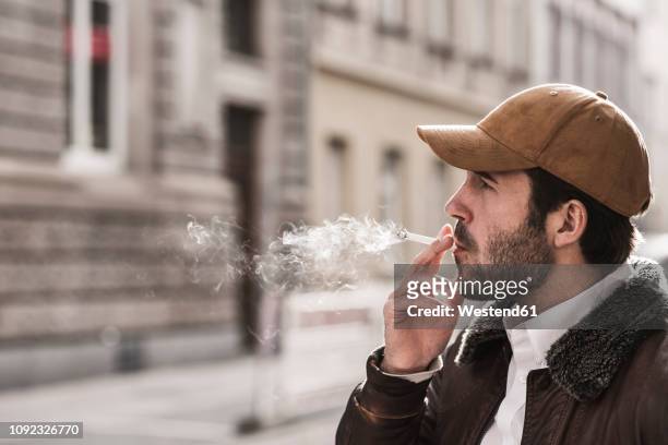 portrait of young man with baseball cap smoking cigarette - cigarette stock pictures, royalty-free photos & images