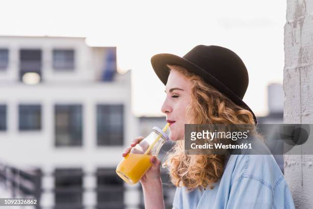 portrait of young woman with hat drinking beverage - orange juice stock-fotos und bilder