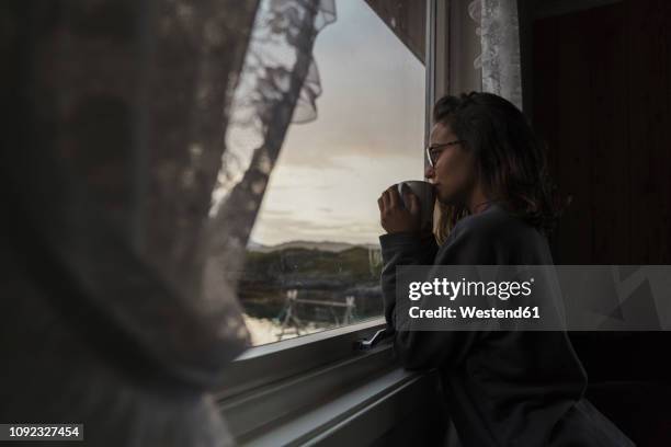 young woman looking out of window, drinking tea - tea outdoor stock pictures, royalty-free photos & images