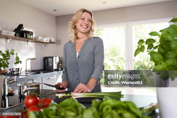 smiling woman cutting spring onions in kitchen - mature woman herbs stock pictures, royalty-free photos & images