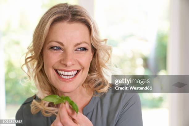 portrait of smiling woman holding basil in kitchen - mature woman herbs stock pictures, royalty-free photos & images