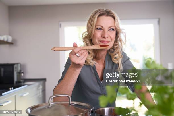 smiling woman cooking in kitchen tasting tomato sauce - speisen und getränke stock-fotos und bilder