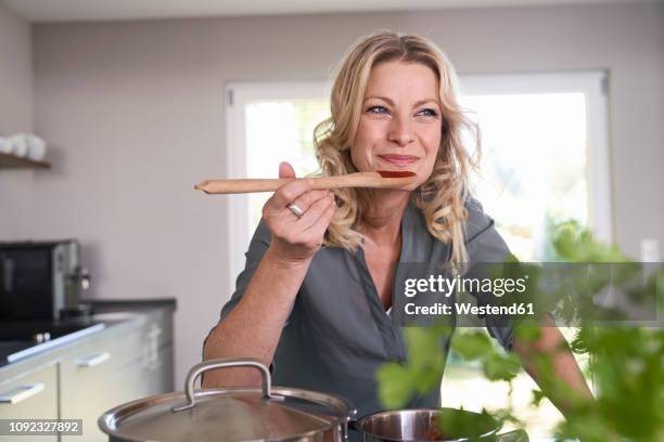 smiling woman cooking in kitchen tasting tomato sauce - cucchiaio di legno foto e immagini stock