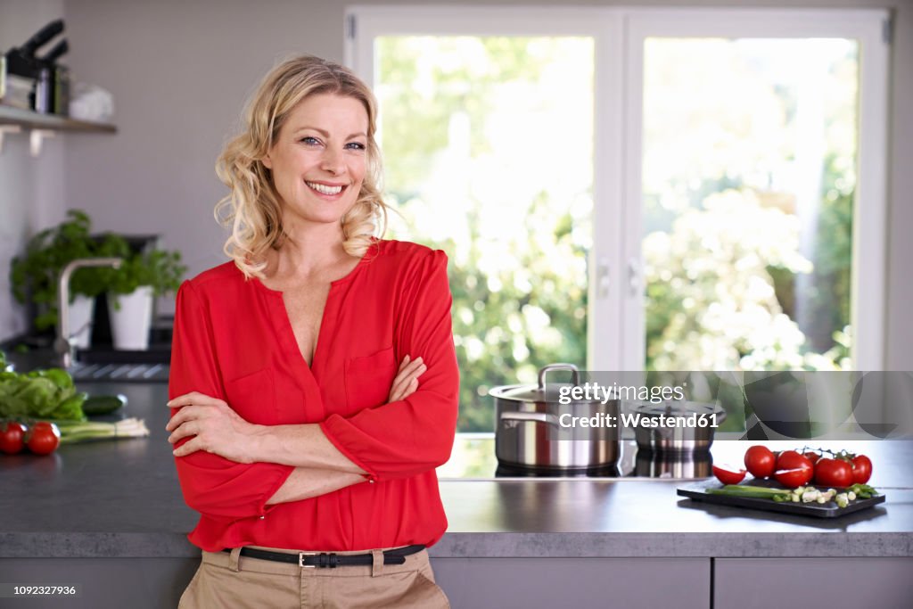 Portrait of smiling woman wearing red blouse standing in kitchen