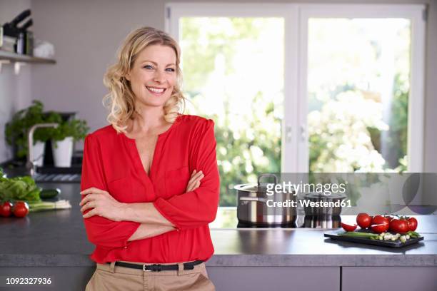 portrait of smiling woman wearing red blouse standing in kitchen - kitchen bench top stock pictures, royalty-free photos & images