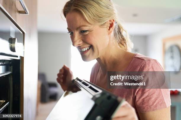 smiling woman cooking in kitchen looking into oven - looking back stock-fotos und bilder