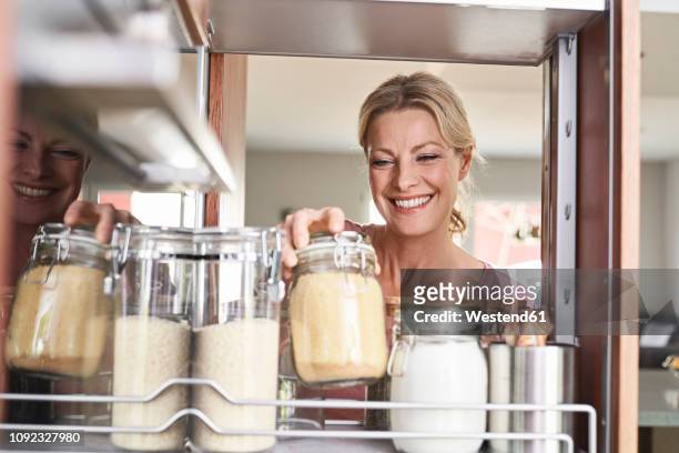 smiling woman in kitchen taking jar from kitchen cabinet - zucchero di canna foto e immagini stock