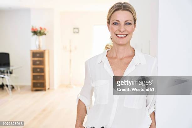 portrait of smiling woman wearing white blouse at home - bluse stock-fotos und bilder
